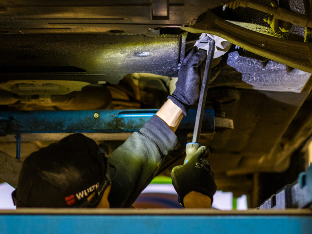 Autonasentaja auton alla työskenetelemässä.