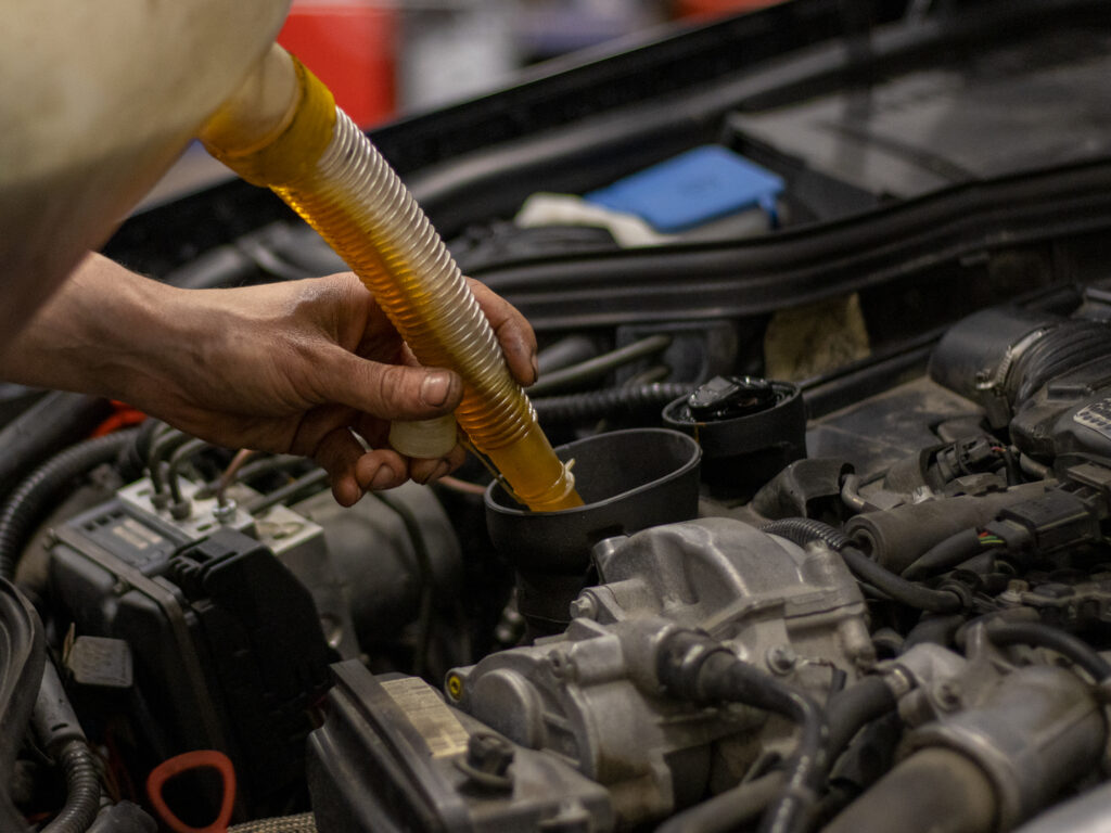Autonasentaja kaataa moottoriöljyä auton moottoriin öljykannun avulla.