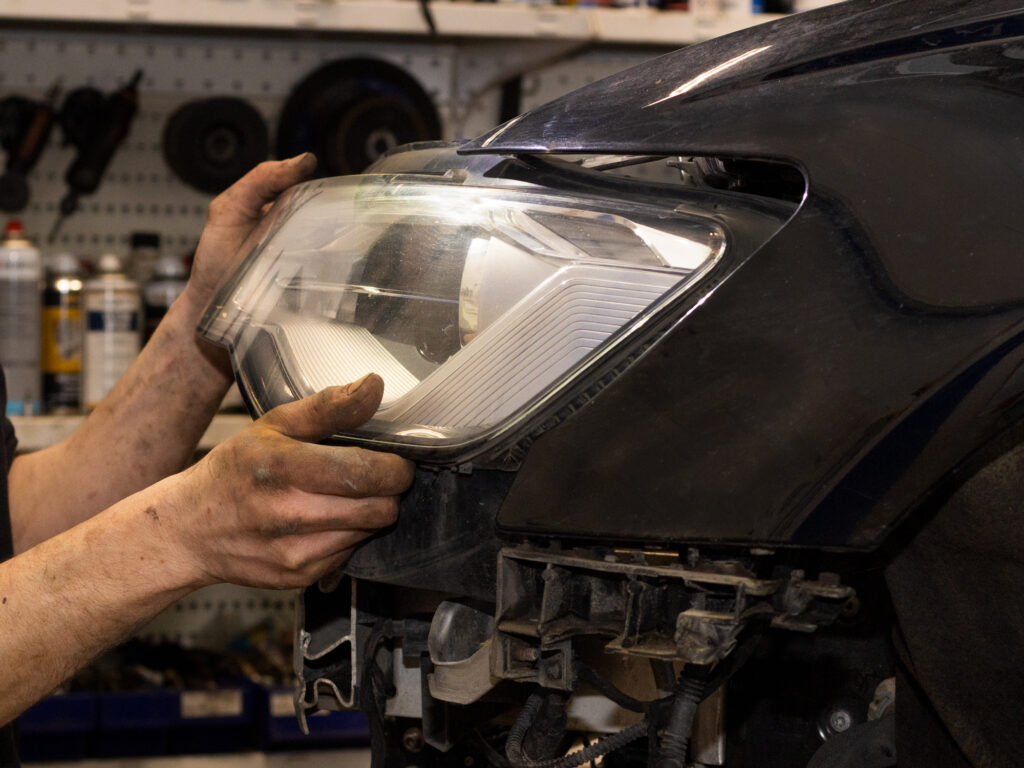 Autonasentaja irroittamassa ajovaloumpiota autosta remonttia varten.